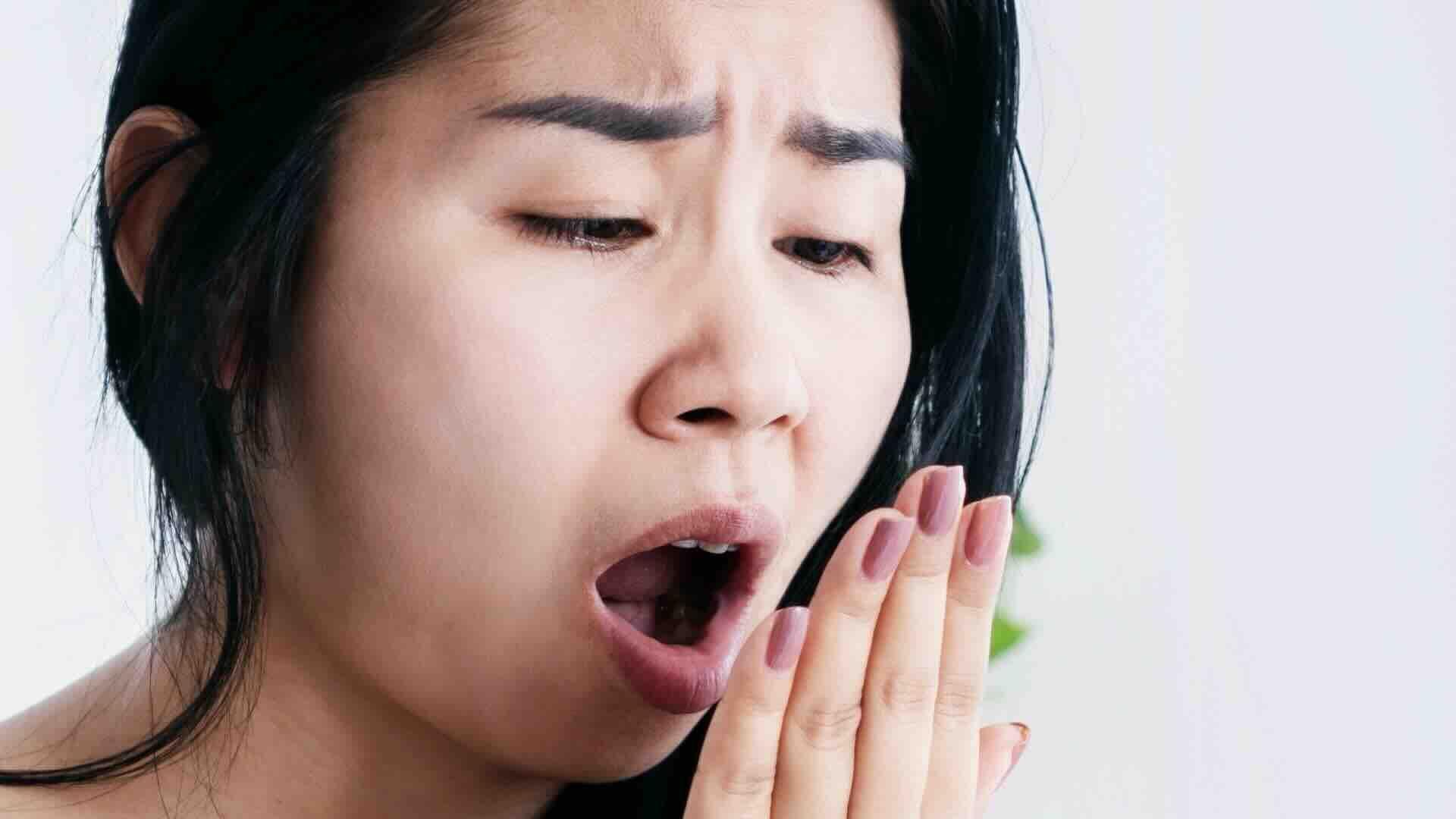 امرأة تضع يدها أمام وجهها وتتنفّس عليها لتفحص رائحة فمها. - Getty Images