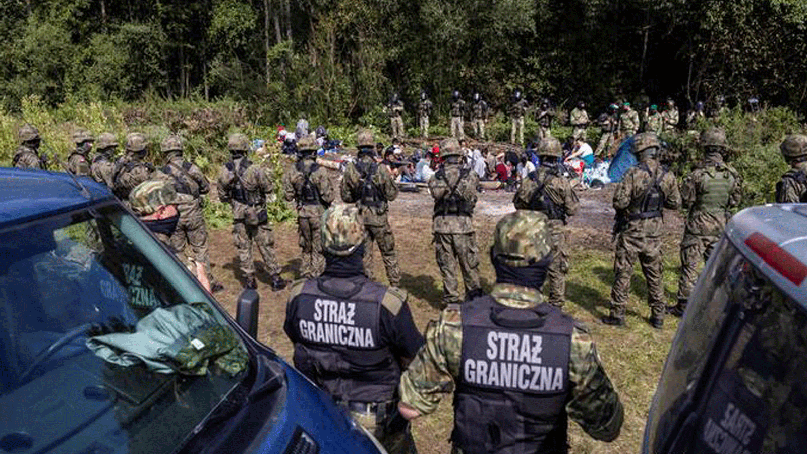 حرس الحدود البولنديون يقفون بمواجهة المهاجرين في قرية أوسنارز غورني الصغيرة، بالقرب من الحدود مع بيلاروسيا. في 20 آب/ أغسطس 2021