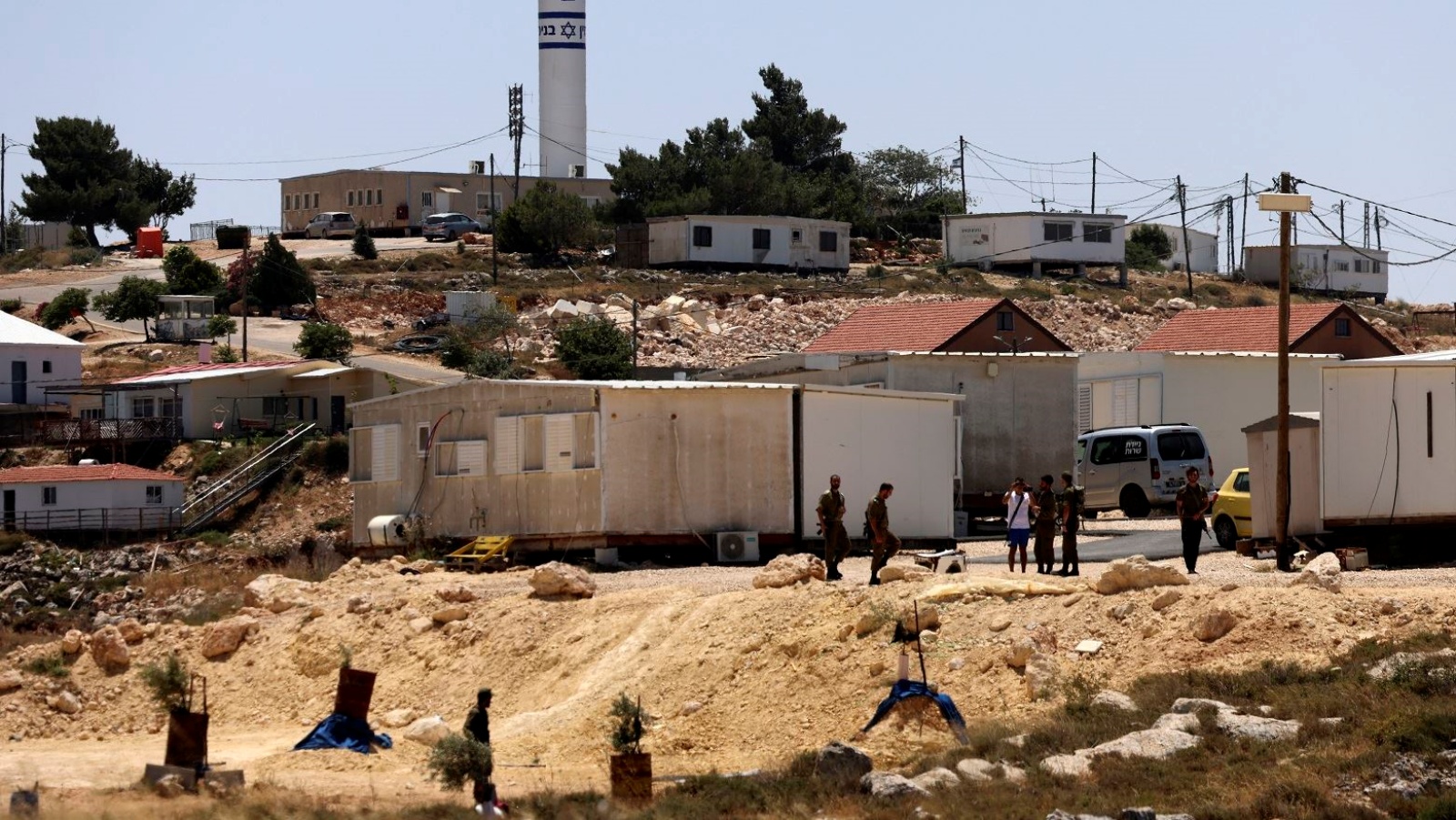 مستوطنون وجنود إسرائيليون يقفون عند مدخل مستوطنة إسرائيلية بالقرب من قرية جالود في الضفة الغربية 31 مايو 2023