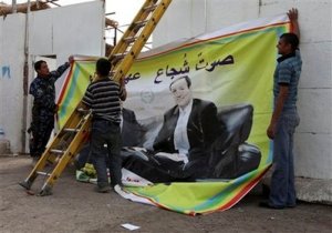 شبان عراقيون يرفعون ملصقاً انتخابياً لعلي الدباغ الناطق بلسان الحكومة