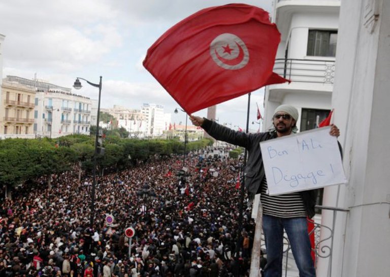 صورة لتونسي يرفع علم بلاده خلال تظاهرة 14 يناير 2011 الحاشدة والتي انتهت برحيل بن علي عن تونس