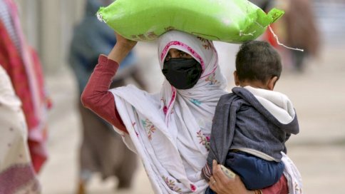 سيدة تحمل طفلها وكيس دقيق من نقطة توزيع في العاصمة الباكستانية 
